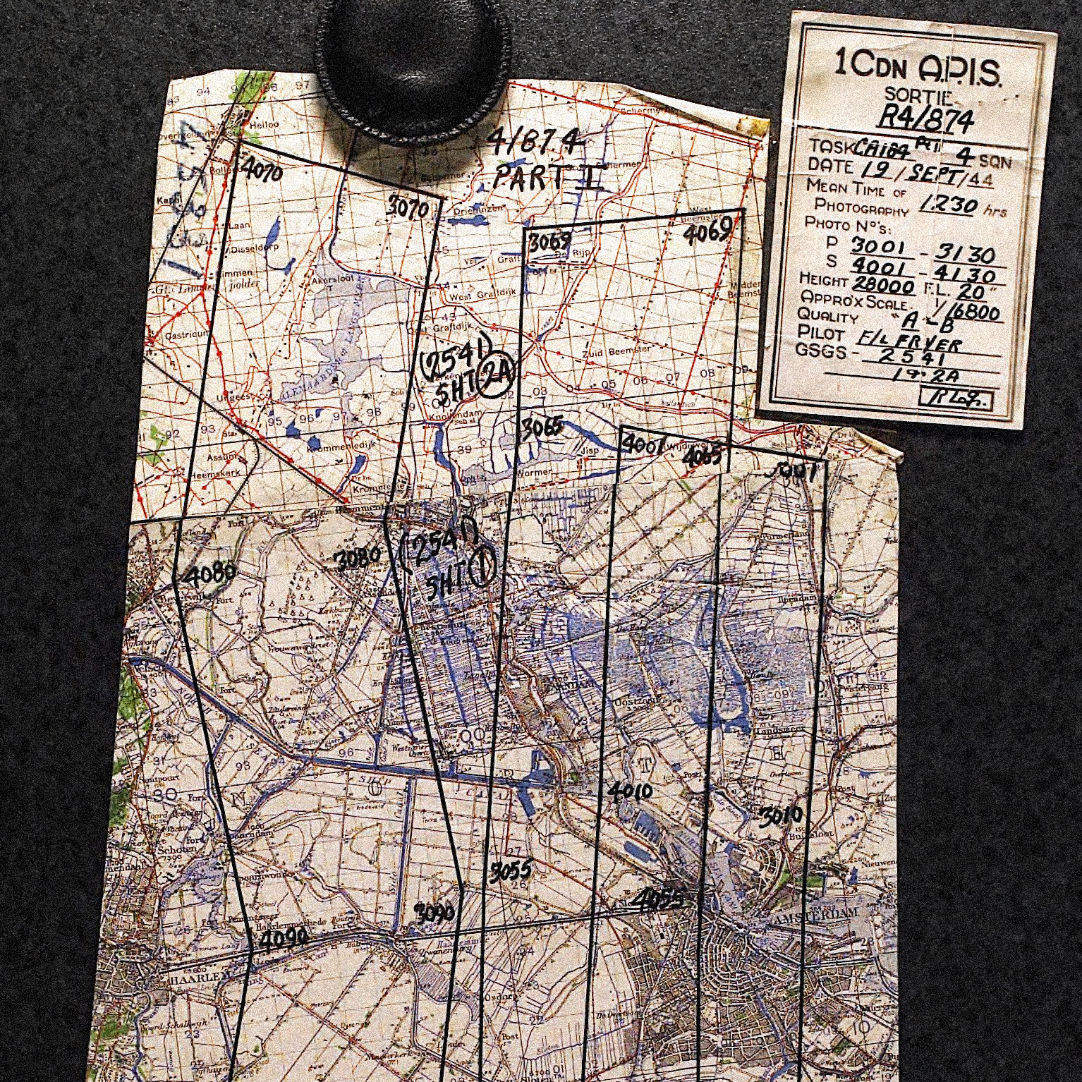 Historische Karte mit eingezeichneten Markierungen auf dunklem Untergrund. Oben rechts liegt ein Schild mit verschiedenen Daten darauf geschrieben.